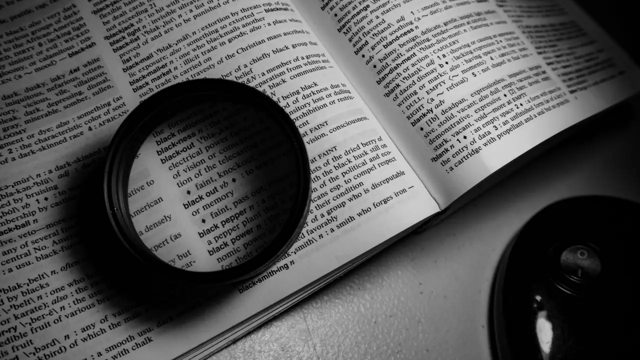 Lente d’ingrandimento appoggiata sulle pagine aperte di un dizionario, in bianco e nero, con le voci ingrandite al centro della lente