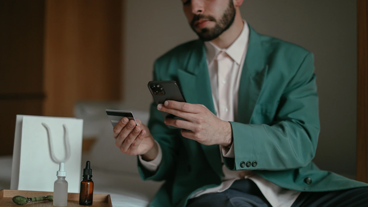 Uomo con giacca verde che tiene in mano una carta bancaria e lo smartphone
