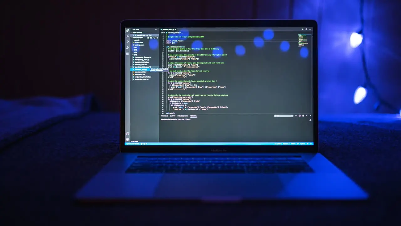Laptop su tessuto scuro con codice su schermo, luce blu e bokeh sullo sfondo